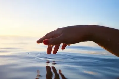 Foto einer Hand über dem Wasser. Dieses Bild veranschaulicht das Gleichgewicht des Wassers in einem Schwimmbecken. 